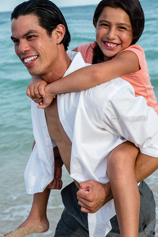 小女孩被她的父亲抱在沙滩上对着镜头微笑
