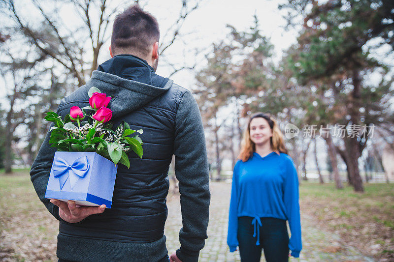男人躲在一束花后面，给女孩一个惊喜。