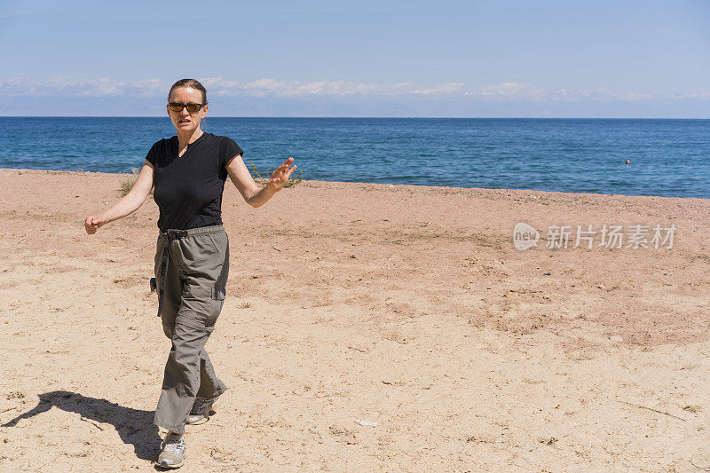 正面的年长妇女，一个游客走在海滩上，享受伊西库尔湖在吉尔吉斯斯坦