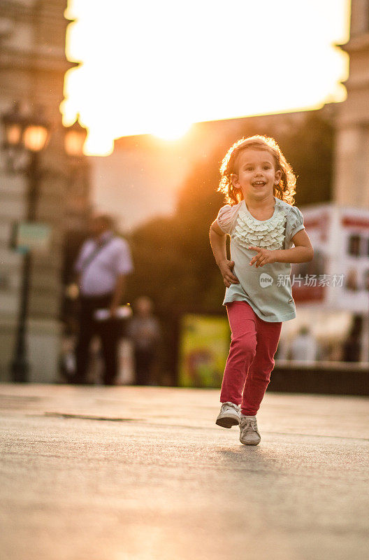 一个快乐的小女孩在金色的夕阳下奔跑在城市里