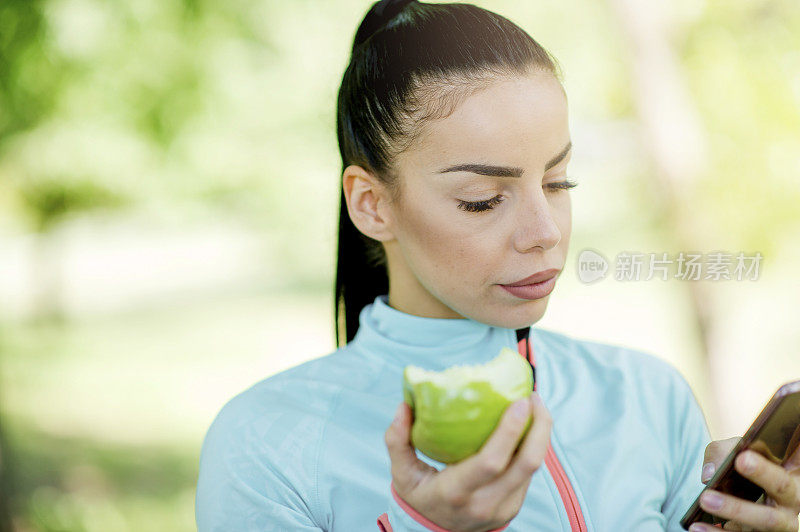 用智能手机吃苹果的女人的肖像