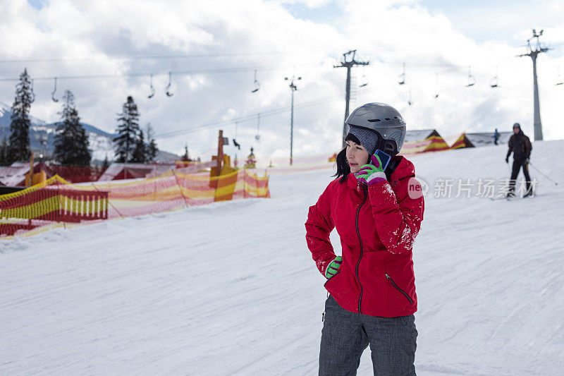 在滑雪场与朋友通电话的女子单板滑雪。