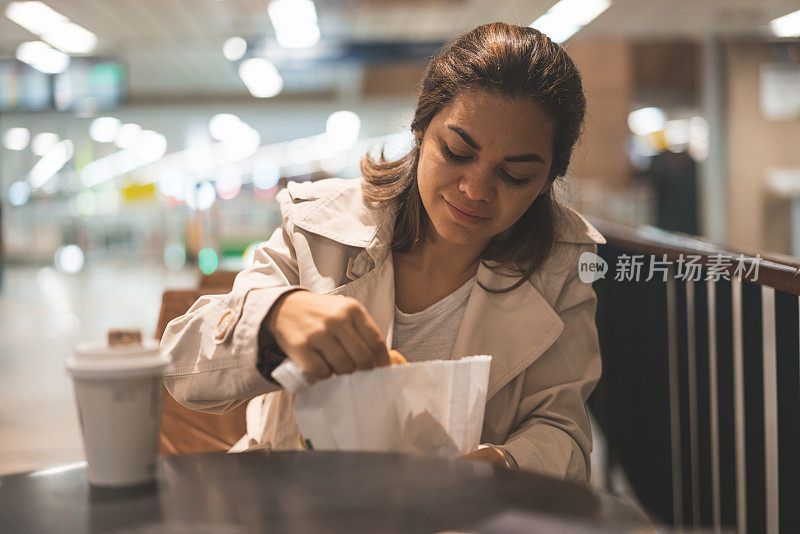 年轻女子喝着咖啡，吃着三明治