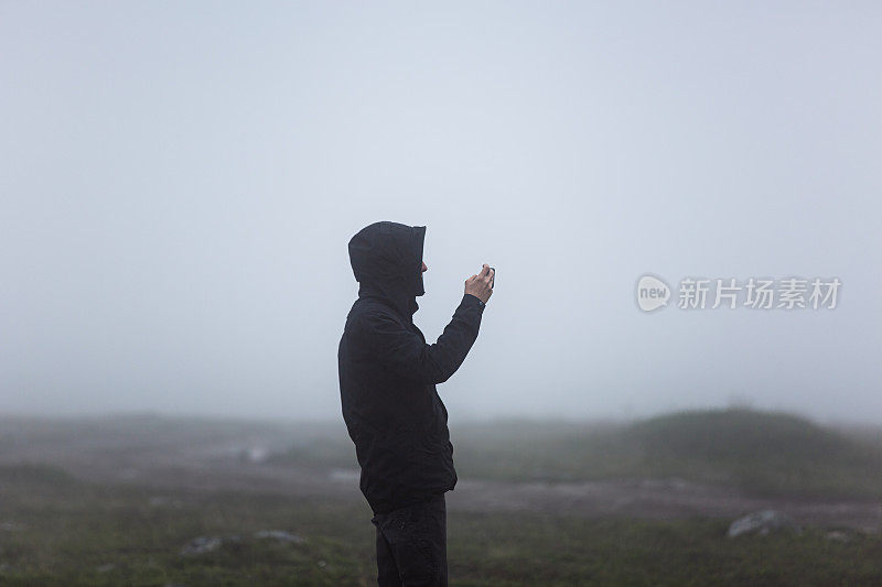 一个穿黑衣服的男人用他的智能手机拍照