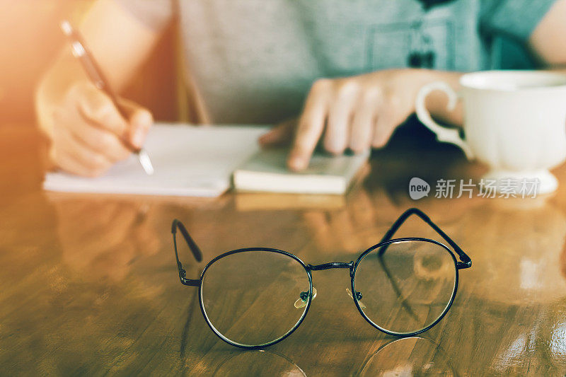 近距离看一位戴着复古眼镜的亚洲年轻女商人的学生拿着一支笔在家里的纸上写信