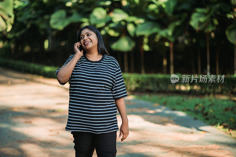 在阳光明媚的日子里，亚裔印度残疾人微笑着用手机聊天和在公园里散步