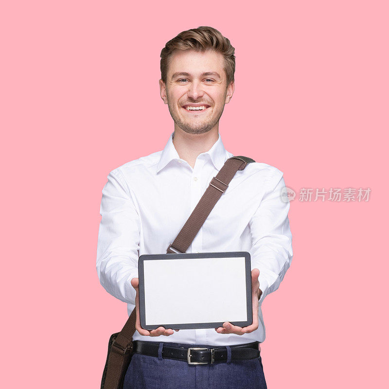 白人年轻男性商务人士站在有色背景前，肩包，手拿包，使用数码平板电脑