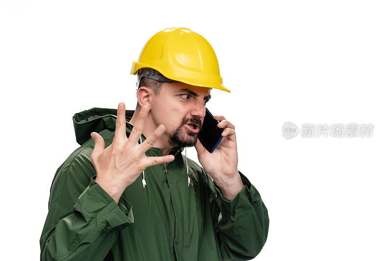 身穿绿色雨衣、头戴安全帽的疯狂工程师在白色背景下使用智能手机