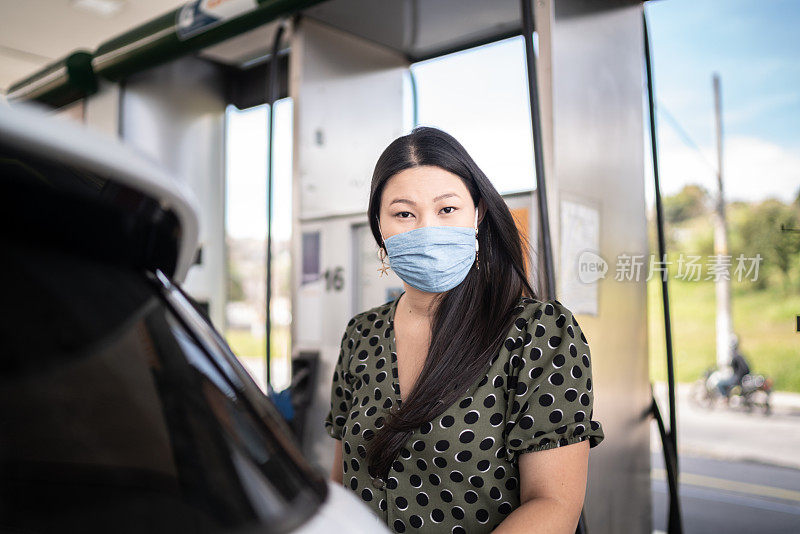 一名年轻女子戴着面具在加油站给她的车加油