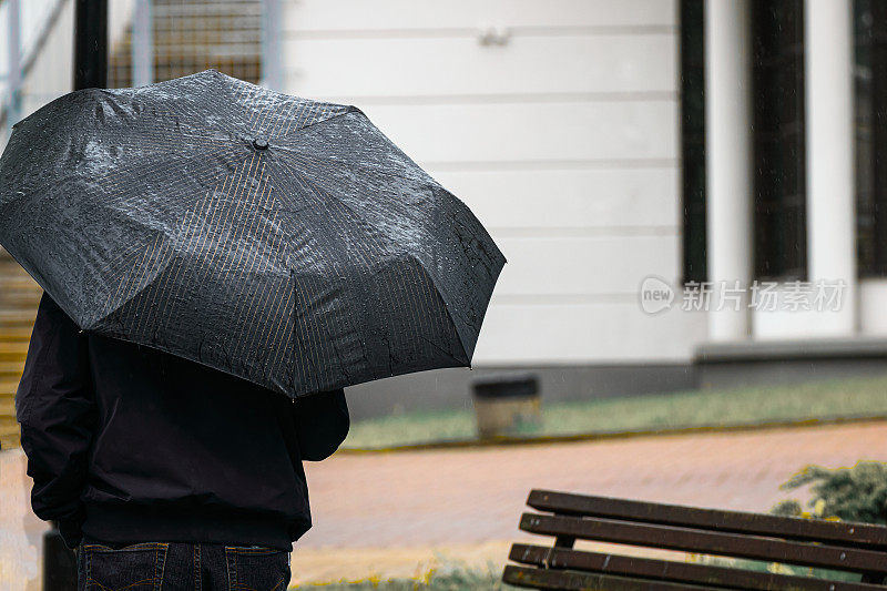雨天，一个男人撑着雨伞在公交车站等车。