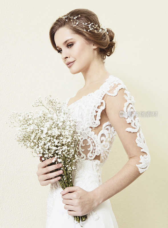 美丽的新娘穿着婚纱站在墙前