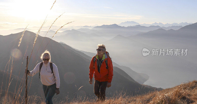 一对成熟的夫妇早晨沿着长满草的山坡徒步旅行