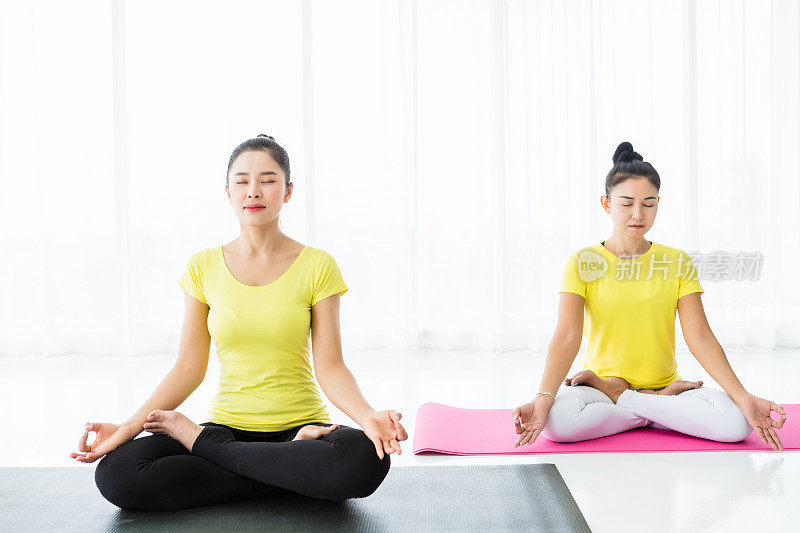 两个年轻的亚洲女性锻炼练习瑜伽在黄色的裙子或姿势与教练和练习冥想健康的生活方式和健康健身的概念在一个健身房。