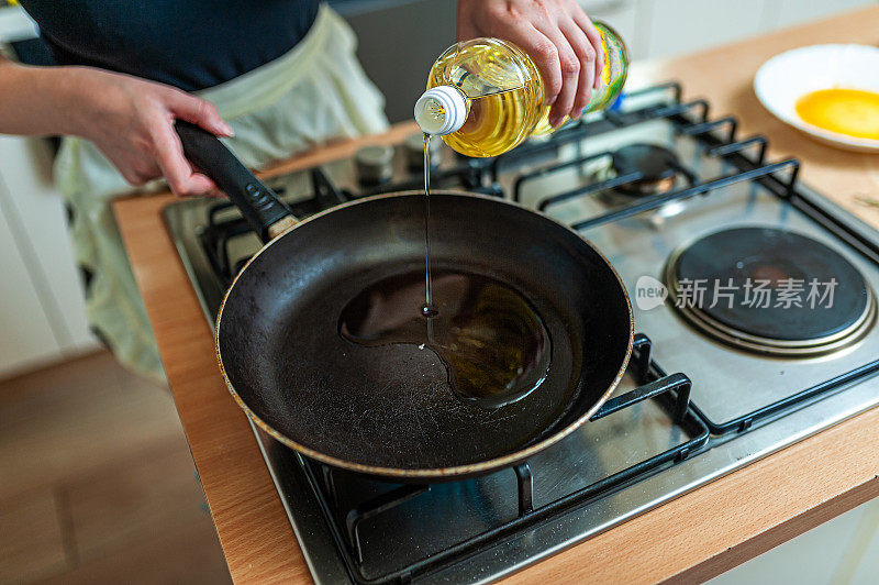 女厨师正在准备一顿饭，同时往平底锅里倒入橄榄油。