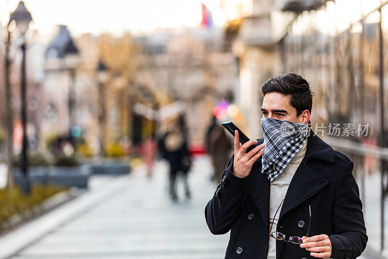 戴大手帕的男子在街上用智能手机当口罩。独立的户外活动。安全城市行走