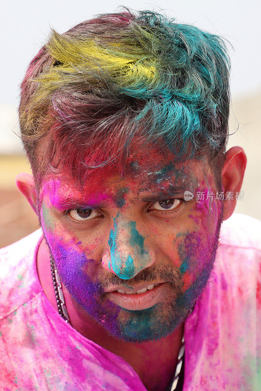 特写画面:一名印度教印度男子身穿库尔塔传统服装，全身涂满油漆粉，在胡里节的色彩和爱漆大战中胡闹，微笑着拍照，看着相机