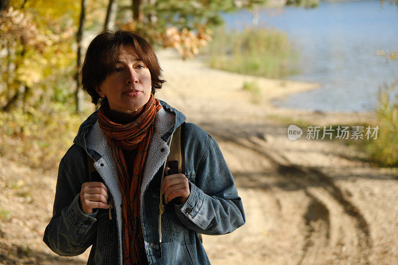 成熟的女人在阳光明媚的秋天自然公园的湖岸