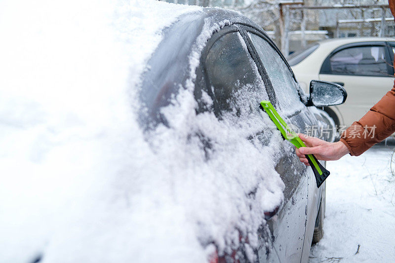 一名男子手里拿着一把刷子，正在擦车窗上的雪。交通的概念，冬天，天气，人和车辆。