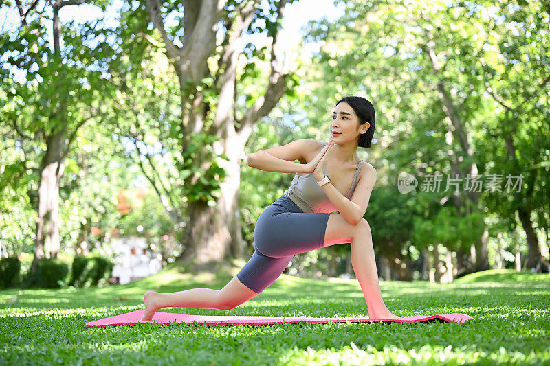 迷人灵活的亚洲妇女在运动服装练习瑜伽在她的瑜伽垫上在花园。
