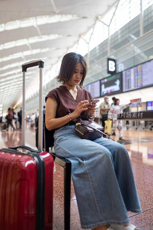 在机场候机楼坐在椅子上使用智能手机的女子