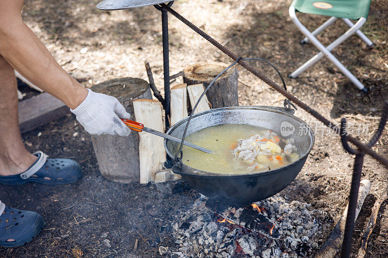 人类在野外用大锅煮饭。在森林的背景下，锅和篝火。露营生活。当地的旅游