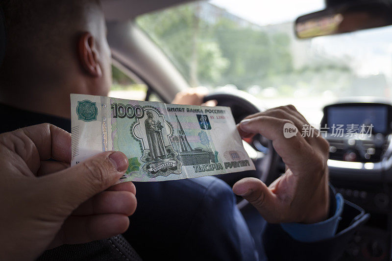 乘客向男性出租车司机支付服务费。客户用卢布支付旅行费用。1000卢布纸币在男性手中