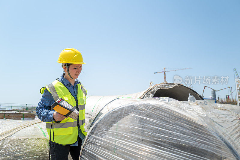 一名亚洲女工在工地的钢管旁用仪器测量数据