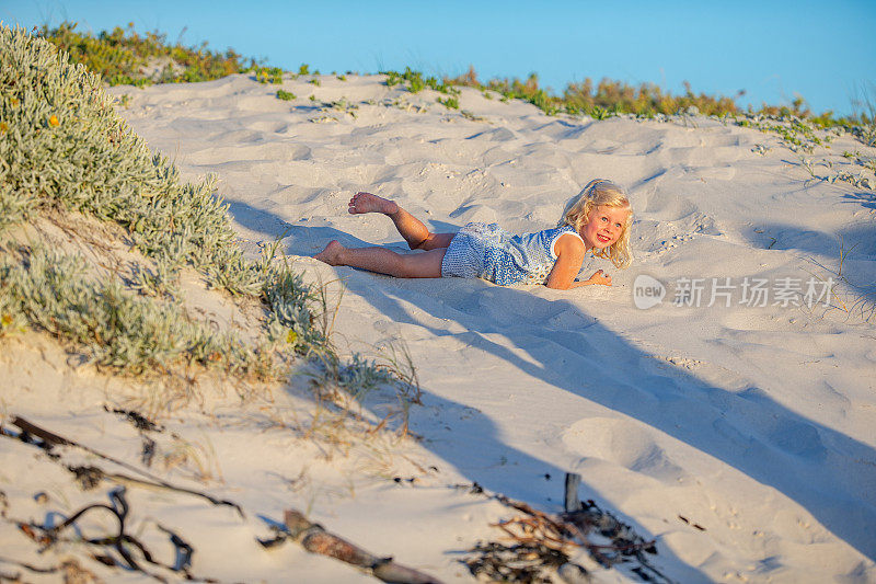 顽皮的小女孩从沙滩上的沙丘上滚下来