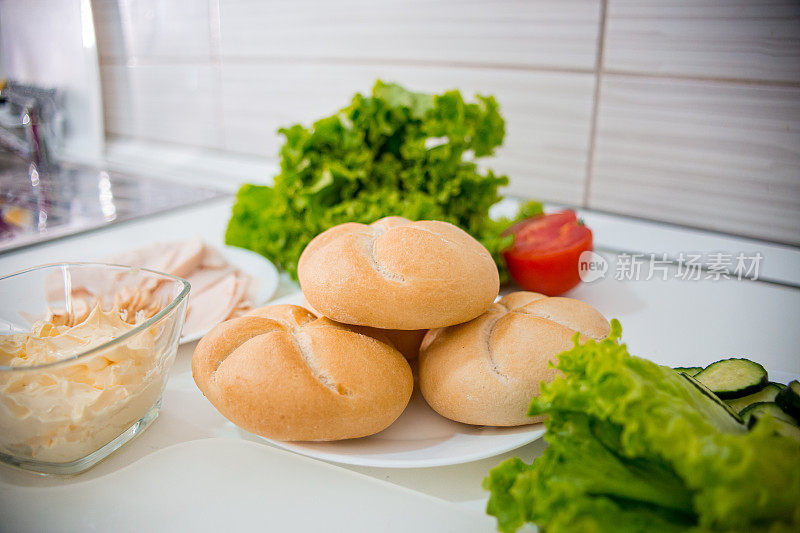 烹饪食品配料。意大利腊肠片，生菜沙拉，奶酪，黄油，面包，小面包，黄瓜，三明治和西红柿。俯视图