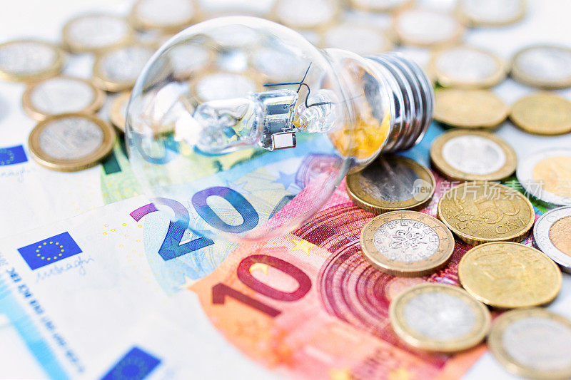 灯泡躺在欧元纸币上，背景是欧元硬币