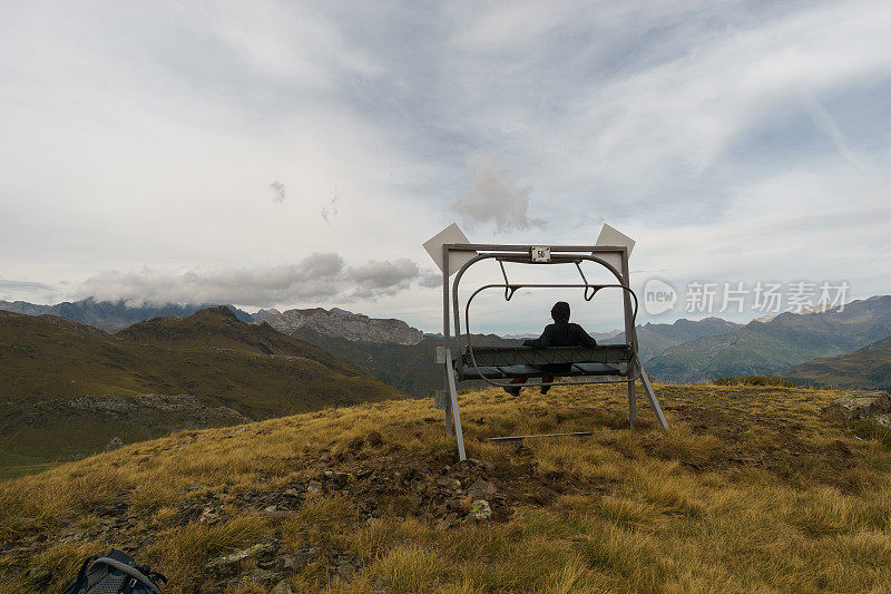 法国新阿基坦，一名徒步旅行者坐在滑雪缆车上的旧长凳上观看加瓦尼附近美丽的山景