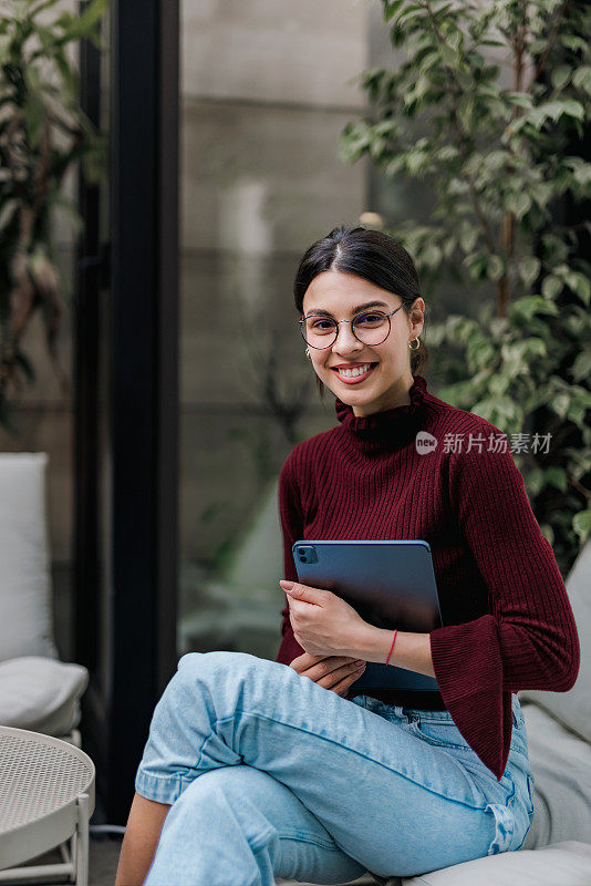一个微笑的女孩的肖像，对着相机摆姿势，拿着平板电脑。