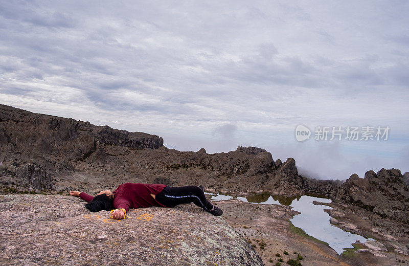 一个拉丁女人躺在一块岩石上，背景是泻湖和岩石山谷