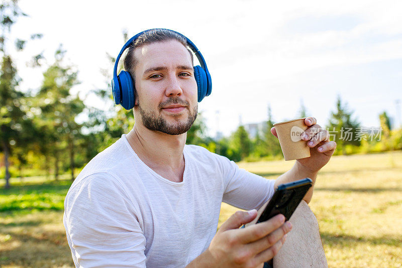 一个快乐的人在夏日公园里穿着白色外套，戴着耳机听音乐