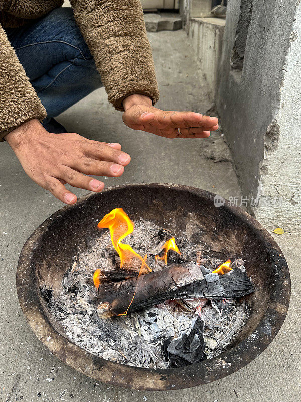 卡代(印度火碗)的特写图像，舞蹈的火焰，灰烬和烟雾，燃烧的木头余烬，无法识别的人温暖的手，抬高的观点，关注前景