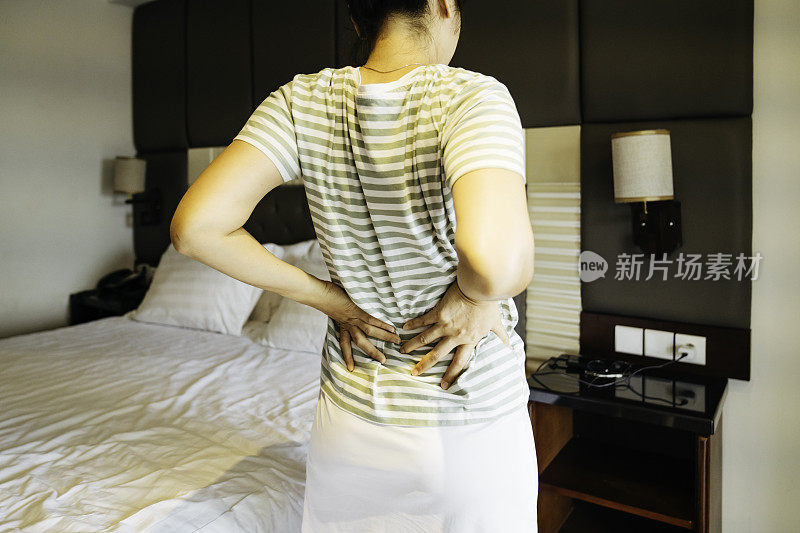 背部疼痛的女人站在卧室在家里的后视图