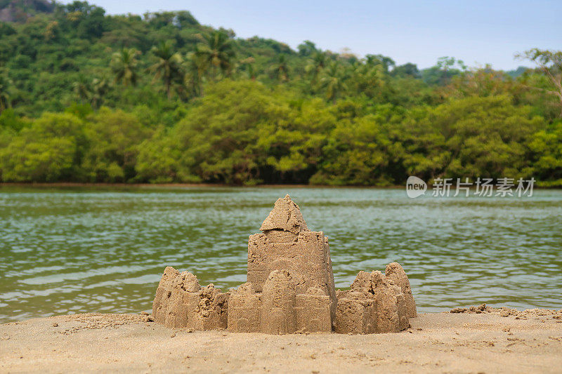 在印度果阿的海滩上建造的复杂沙堡堡垒图像，用桶和铲子制作，并修改为围绕外部创建一堵墙，背景是大海，远距离图像