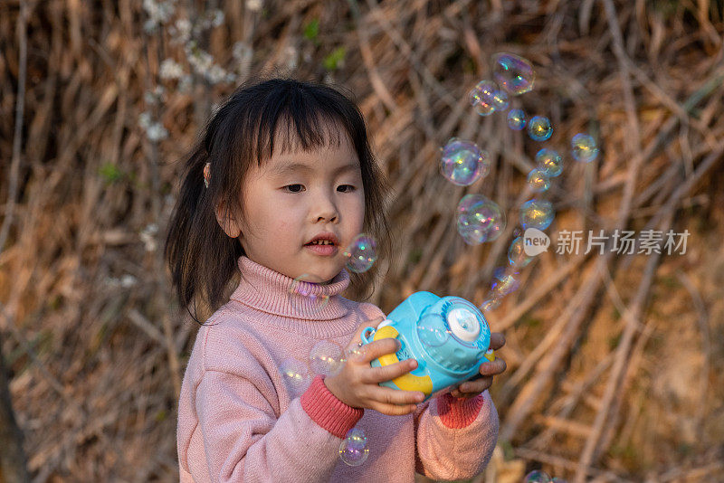 一个小女孩在梅园里用玩具吹泡泡