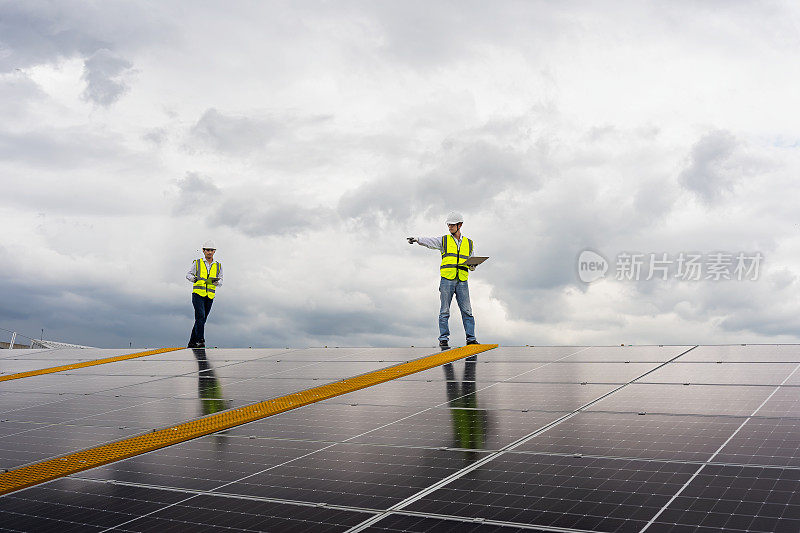 两个年轻的亚洲工程师在工厂屋顶检查太阳能电池板的安装情况，对照电脑中的图纸检查太阳能电池板的安装情况。