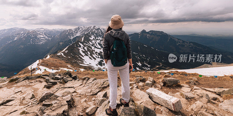 女人的女性肖像，谁在山中旅行。在户外徒步旅行的人。生活方式人物摄影，旅游理念。女孩是背包客，背包里装着旅游装备，从后面看。女孩手里拿着手机