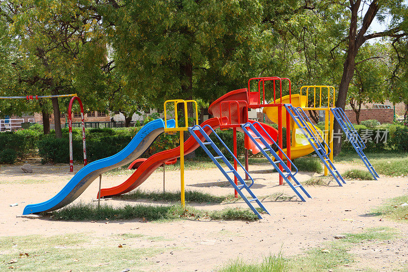 公园儿童游乐场的形象，多色，红色，黄色和蓝色的金属滑梯游乐设备，硬泥地板，注重前景，健康和安全的理念