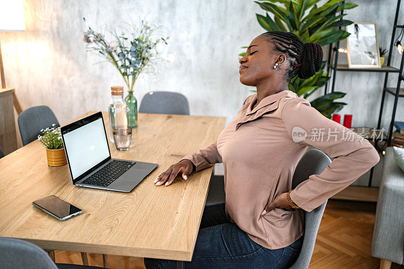 黑人女性在家里用笔记本电脑工作时背部疼痛