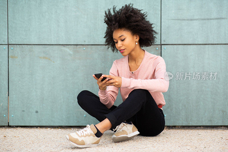 一个非裔美国女人坐在外面的地板上看手机