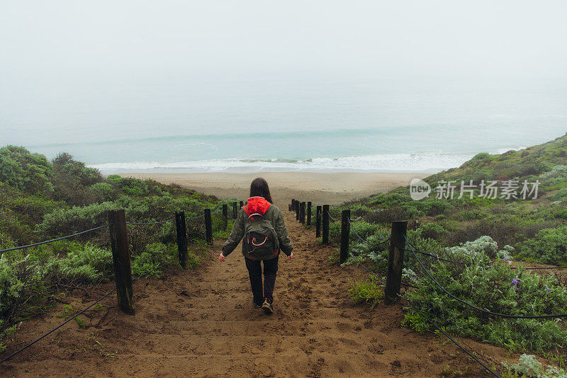 一名女子在考虑下雨天的事，她走在加州旧金山的海滩上