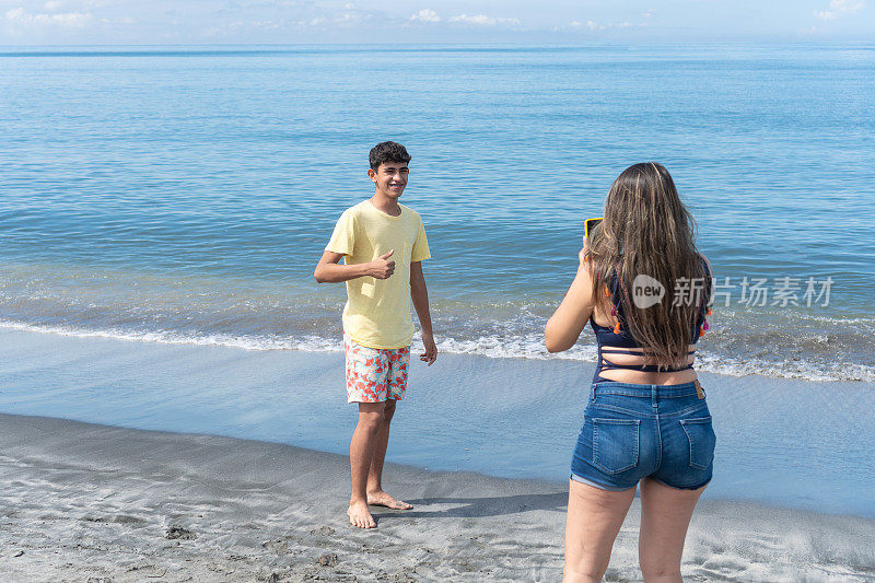 一位拉丁裔母亲在海滩上给儿子拍照