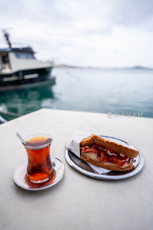 餐桌上的面包和土耳其红茶是前景的焦点，前景的大海和渔船是背景的垂行