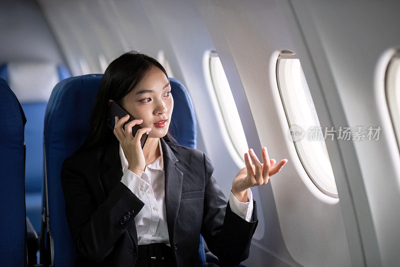 亚洲年轻的成功女企业家或女企业家在飞机上穿着正装，坐在商务舱的座位上，在飞行中使用智能手机。旅游与商务理念