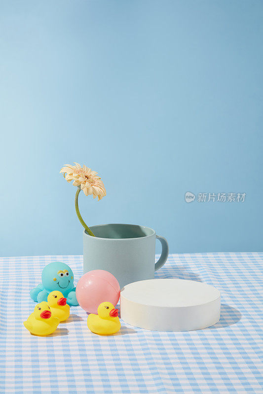 正面照片与空白的圆形讲台展示产品，周围有几个婴儿沐浴玩具和一个蓝色的杯子里有一朵花。用于展示或展示的照片