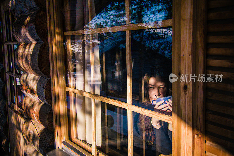 年轻女子在村舍喝茶和透过窗户看