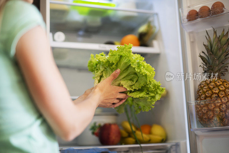 陌生女性从冰箱里拿绿色沙拉。